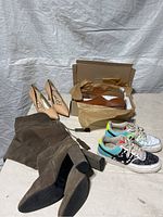Lot of four pairs of women's footwear photographed together on a gray backdrop including brown Madewell boots, nude heels, and two pairs of Nike sneakers.
