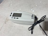 Show top and side angle of X-Rite Spectrodensitometer with cable on a light surface, device powering on shown on LCD.