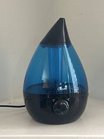 Front view of blue and black Crane humidifier showing the dial and logo on the water tank.