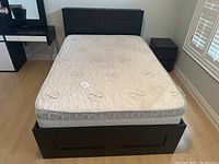 Front view of the IKEA bed frame showing mattress on top and headboard, with storage drawers visible in the frame base