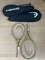 Two Head PCT Fire tennis racquets with white grips and lime green frames and their two black carrying cases with Head branding