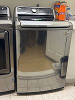 Front view of stainless steel top load washer next to dryer and detergent on shelf