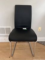 Front view of the black vinyl and chrome frame chair against a wall with vent and outlet visible.