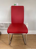 Front view of red vinyl chair with chrome cantilever legs against white wall and hardwood floor