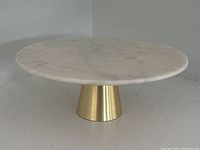 Front view of the round marble cake stand with gold base on a plain neutral background.