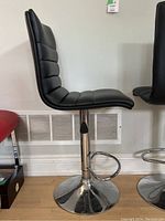 Side profile view of one black vinyl bar stool showing padded seat, backrest, and chrome pedestal base with footrest.