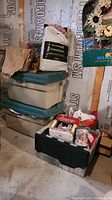 Stacked plastic storage bins and bags containing Christmas decoration items.