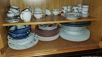 Shelf with assorted cups, saucers, plates, and serving dishes of various patterns and colors