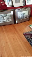 Two framed architectural wall art prints resting on a wooden floor showing overall lot contents.