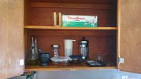 Kitchen cabinet shelf with assorted kitchen prep tools including Bodum French press, oil dispenser bottle, mortar and pestle, white plastic bowls, and Moulinex food chopper box.