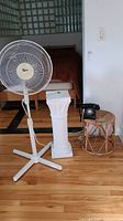Rotary phone, wicker table, plant stand, and standing fan displayed on wooden floor