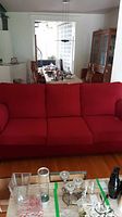 Front view of red three-seater sofa with three seat cushions and attached back cushions.