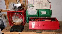 Red metal toolbox with various hand tools inside and green plastic bins in the background on a wooden workbench.