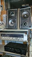 Full view showing two vintage stereo speakers placed on top of a wood surface. Below the speakers is a Kenwood stereo receiver with control knobs and display. Beneath receiver is a JVC cassette deck in black.