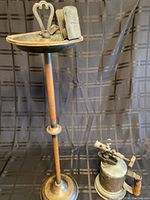 Full view of the vintage brass ashtray stand and copper blowtorch on a plain black background.