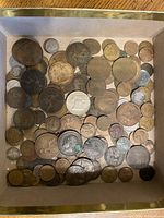 Top-down view of a box filled with a large assortment of old circulated coins in different sizes and metals, some heavily tarnished and worn.