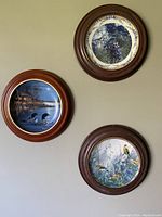 Three round framed wall dishes with bird themes arranged on a wall, showing overall set condition and display style