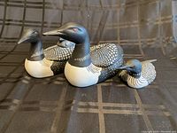 Front and side view of two ceramic loons and one smaller carved wood loon figurine grouped together on a dark fabric background.