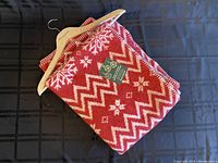 Folded red blanket with white zigzag and snowflake patterns on a hanger.