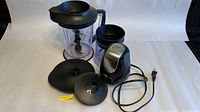 Ninja food processor with clear pitcher, two lids, and motor base with power cable laying on white background.
