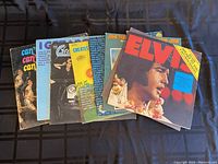 View of seven vintage vinyl record albums stacked side-by-side with various colorful covers, including a prominent Elvis Presley album.