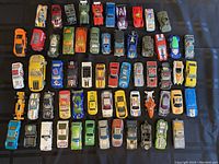 Top view of 50 toy cars arranged in rows on a dark surface, showing various colors and wear levels.