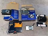 Overview of five cameras, boxes, cases and cables on carpet