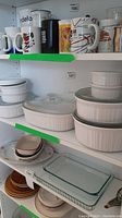 Shelf of Corning bakeware including white dishes with glass lids, bowls, and mugs above