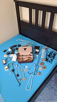 Complete overview of costume jewelry items arranged on a blue surface showing jewelry case, necklaces, pendants, and earrings