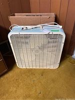 Front view of the Electrohome box fan with original box behind it, showing the fan body and power cord.