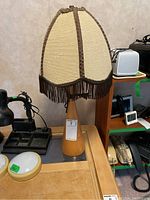 Front view of the table lamp showing wooden base and beige fabric shade with dark brown trim and fringe