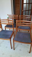 Four chairs grouped, front three-quarter view showing ladder-back frames and blue upholstered seats