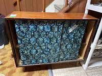 Front view of vintage shelf unit showing blue painted sliding doors with a detailed pattern and wooden top surface.