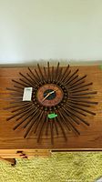 Full view of the medium brown plastic sunburst wall clock laid flat on wooden surface.