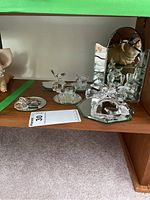 Shelf with Swarovski and glass animal figurines placed on mirrored bases, showing clear faceted crystal details and some gold accents on pig figurine.