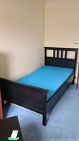 View of the twin bed from the side, showing blue foam mattress and dark wood frame with headboard and footboard.