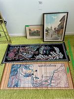 Photo showing two framed wall art prints, black fabric embroidered hanging, and two bamboo scrolls laid out on carpet.