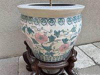 Ceramic planter pot with Asian floral and vine motifs in pastel colors on an outdoor stone surface.