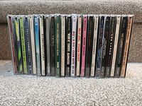 Twenty-three CDs in jewel cases showing spines with titles such as Earth Wind & Fire Greatest Hits, Classic Hits from the 60s, Grammy Nominees 2003, Andy Williams Christmas Album, Billy Joel Storm Front, and others.