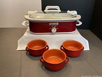 Red rectangular Crock-Pot slow cooker with removable stoneware insert and 3 red ceramic bowls in front.