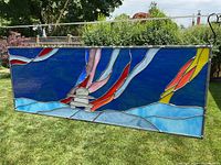 Front view of stained glass panel showing Inukshuk with colorful Northern Lights ribbons and snowy ground in a metal frame with hooks for hanging.