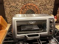 Front view of silver Hamilton Beach toaster oven on stove, showing closed glass door with handle and brand label.