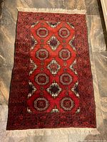 Full view of the handwoven Persian rug laid flat on floor showing red central field with geometric medallions and intricate border.
