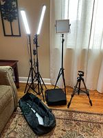 Full view of one Velbon tripod, two LED vertical bar lights on stands that are lit, one square LED light on stand unlit, and black bag on floor.