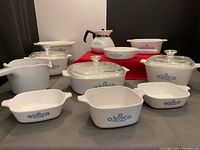 Photo showing the full assortment of Corning Ware cookware including baking dishes, measuring jug, small pot, pan, and coffee pot with the Cornflower pattern.