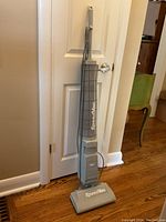 Full front profile of the IONA SpeedVac stick vacuum showing its slim, upright design leaning against a door.
