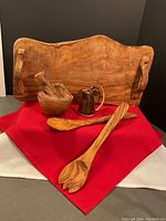 Wide view showing all items in the lot including the charcuterie board, mortar and pestle, two salad spoons, and ceramic pitcher on red cloth
