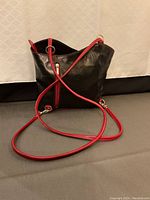 Black Italian leather purse with red leather straps displayed on gray and white backgrounds.