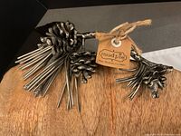 Close-up view of metal handles shaped like pinecones with pine needle details, showing tag from brand 'Mud Pie'.