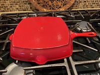 Photo of red enameled cast iron grill pan with lid on gas stove, showing square shape and handle